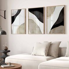 three abstract paintings hang on the wall above a white couch in a living room area