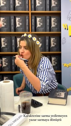 a woman sitting at a table in front of a bookshelf holding a cup