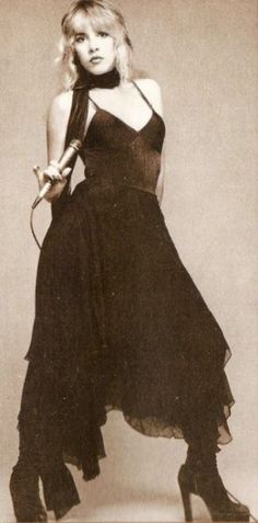 an old photo of a woman in a black dress and high heeled boots, posing for the camera