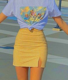 a woman wearing a white shirt and yellow plaid skirt with her hands on her hips