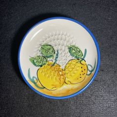 a white and blue bowl with two yellow tomatoes on it's side, sitting on a black surface