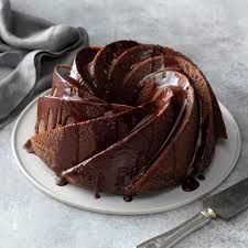 a bundt cake with chocolate icing on a white plate next to a knife