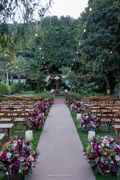 an outdoor wedding ceremony setup with wooden chairs and floral centerpieces on the aisle