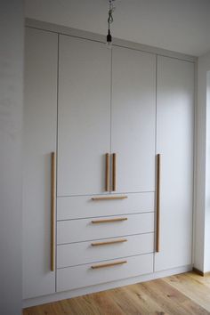 an empty room with white cupboards and wood handles on the doors, in front of a window