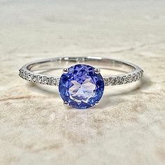 Beautiful 14 karat white gold solitaire cocktail ring featuring a natural 6 mm round tanzanite, weighing approximately 0.75 carat. It is shouldered by approximately 0.09 carat of diamonds. Tanzanite is the birthstone for December. Diamond is the birthstone for April. Size 7 resizable. Birthstone: April/December Condition: Brand New. - 14 day return policy, no questions asked. - Free insured shipping in the US. - International shipping available. - Courtesy ring sizing included. Feel free to call Modern Tanzanite Round Rings, Round Tanzanite Sapphire Ring With Accent Stones, Tanzanite Round Ring As A Gift, Round Tanzanite Rings For Gifts, Tanzanite Round Rings As Gift, Classic Round Tanzanite Rings, Brilliant Cut Tanzanite Sapphire Ring, Solitaire Tanzanite Jewelry In Round Cut, Solitaire Tanzanite Round Cut Jewelry