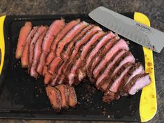 sliced meat sitting on top of a black tray next to a yellow spatula and knife