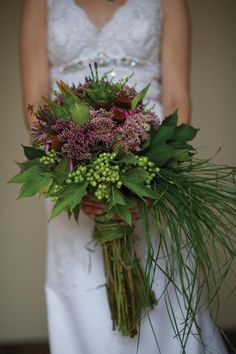 a bride holding a bouquet of flowers and greenery