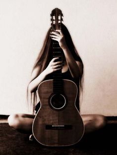 a woman sitting on the floor with her guitar in front of her face and hands behind her head