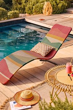 an outdoor lounge chair next to a pool with a straw hat on it and a book