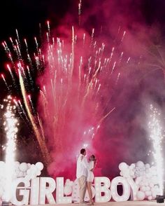 two people standing in front of a sign that says girl boy with fireworks behind them