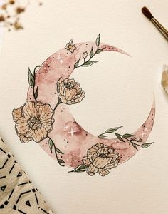 a watercolor painting of a crescent moon with flowers on it and paintbrush next to it