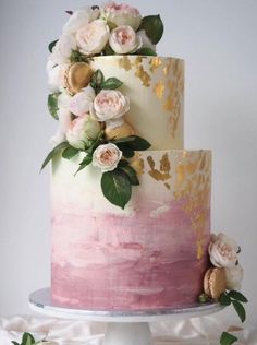 a three tiered cake with pink and gold frosting, topped with flowers on top