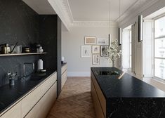 an empty kitchen with black counter tops and wooden flooring in front of large windows