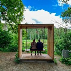 two people sitting on a bench in the middle of a forest, looking out into the distance