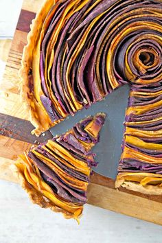 a cake with purple and yellow swirled icing on a cutting board next to a knife