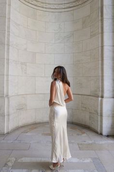 a woman standing in front of a stone wall wearing a white dress and high heels