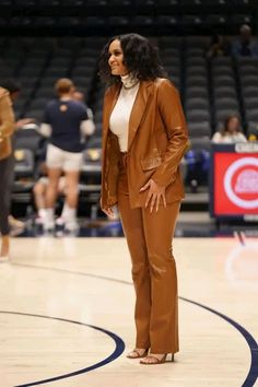 a woman standing on top of a basketball court wearing a brown suit and white shirt