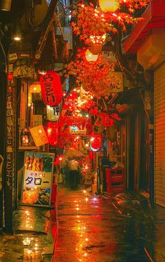 an alley way with lights and lanterns on the trees in the rain at night time