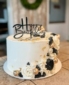 a white cake with black and gold decorations on it that says happy birthday written in frosting