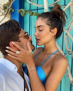 a man and woman kissing each other in front of a blue wall with white branches