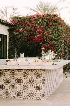 a table with food on it sitting in front of some bushes and flowers near a building