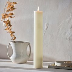 a white candle sitting on top of a table next to a vase