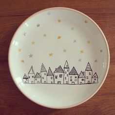 a white plate with houses painted on the side and stars in the sky above it