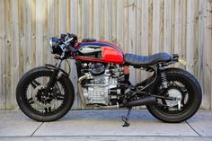 a red and black motorcycle parked next to a wooden fence