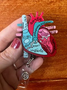 a hand holding a heart shaped clip with words on it and a keychain attached to the clip