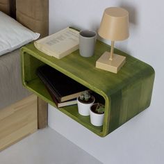 a green shelf with books and cups on it next to a lamp, bookcase and bed