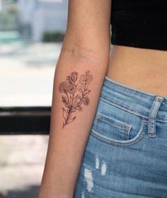 a woman's arm with flowers on it and a small tattoo behind the arm