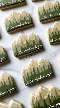 cookies decorated with mountains and trees are on a marble countertop for someone to write their names