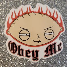 a sticker with the words obey me on it in red and black lettering, sitting on a silver surface