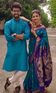 two people standing next to each other in front of some trees and bushes with one person wearing a blue sari