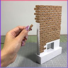 a hand is holding a piece of paper next to a model house made out of bricks