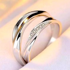 two white gold wedding rings with diamonds on top of each other, sitting on a white cloth