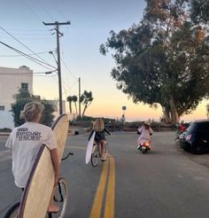 two people riding bikes with surfboards on the back and one person holding a surfboard