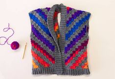 a crocheted vest and knitting needles on a white surface