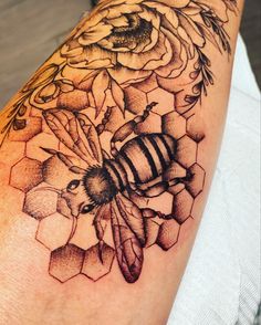 a tattoo on the arm of a woman with a bee and flowers in front of her