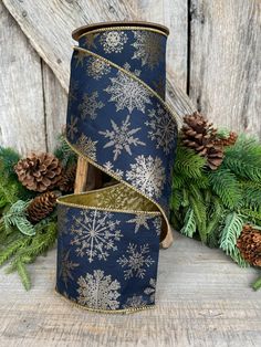 a blue and gold christmas ribbon with snowflakes on it next to pine cones