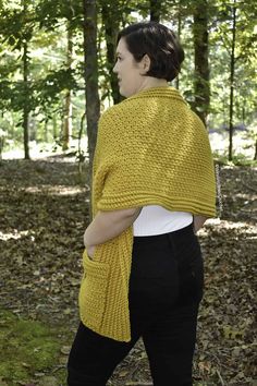 a woman is walking through the woods wearing a yellow knitted shawl over her shoulders