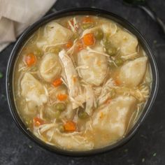 a bowl filled with chicken and dumplings on top of a black table next to a napkin