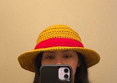 a woman taking a selfie in front of a wall wearing a yellow and red hat