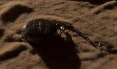 an old pocket watch is laying on the sand with its chain still attached to it