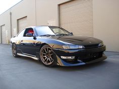 a black car parked in front of a garage door next to a wall with roller doors