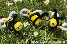 three stuffed bees are in the grass with daisies