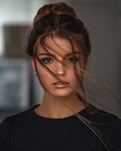 a woman with her hair blowing in the wind and looking at the camera while wearing a black shirt