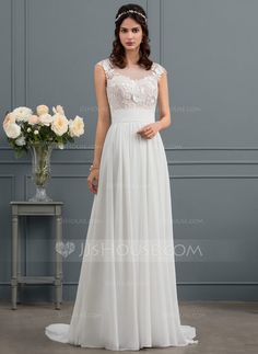 a woman wearing a white dress standing in front of a vase with flowers on it