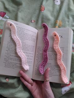 two crocheted bookmarks in the shape of worms on top of an open book