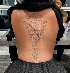 the back of a woman with a butterfly tattoo on her lower back, sitting at a table